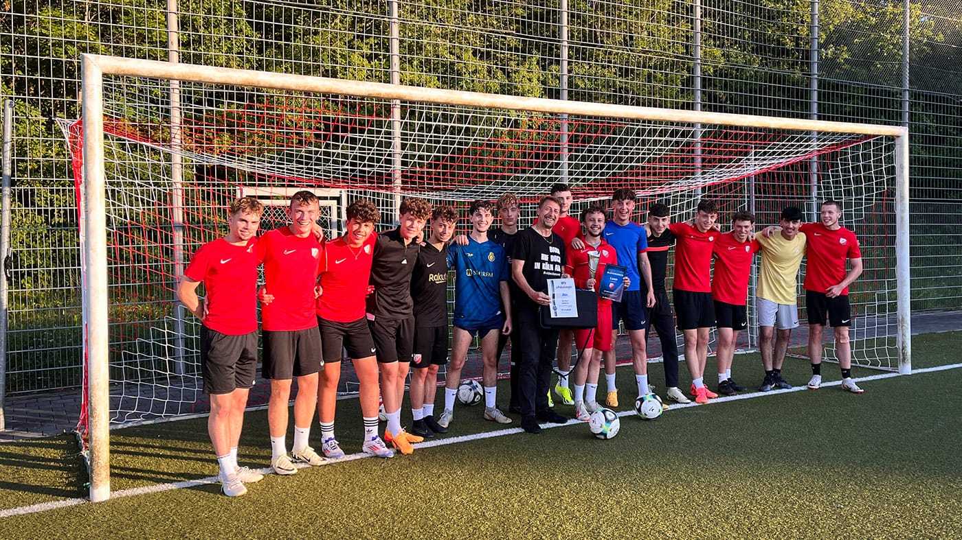 A group of young soccer players stand in front of a goal on a soccer field and pose for a photo.